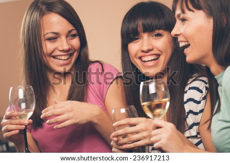 Cheerful young female friends with wine glasses enjoying a conversation on sofa at home