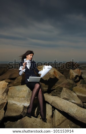 Business lady sitting on the rocks by the sea, against the backdrop of a cloudy sky.