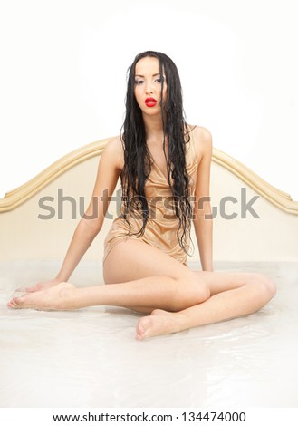 Beautiful girl in wet clothes and wet hair sitting in the white water on a white background.