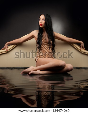 Girl with wet hair and wet clothes sitting in the black water on a black background.