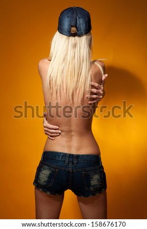 Half-naked blonde in shorts standing with her back on a yellow background