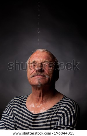 Portrait of a wet man on whom pours water on a dark background.