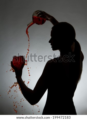 Woman pouring red wine from bottle into a glass on a gray background.