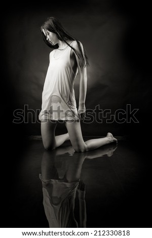 Girl in a white shirt is on his knees in water on a black background.