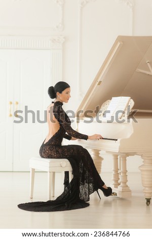 Beautiful girl in a long black dress sitting at the piano.
