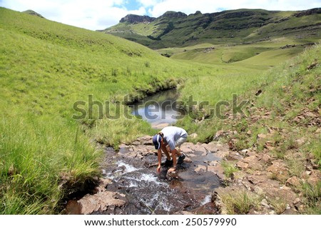 Hiker drinking fresh mountain water from a stream.