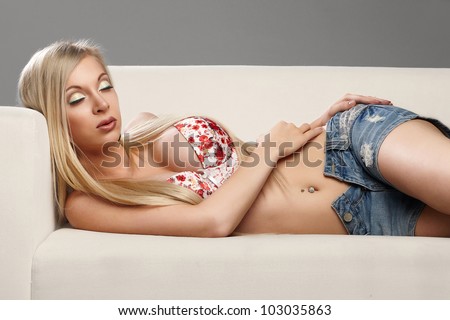 Beautiful sexy blonde with bright make-up is on a white couch in lingerie and in shorts