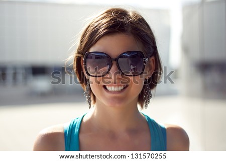 brunette girl in glasses smiling outdoors on a sunny day in a short haircut