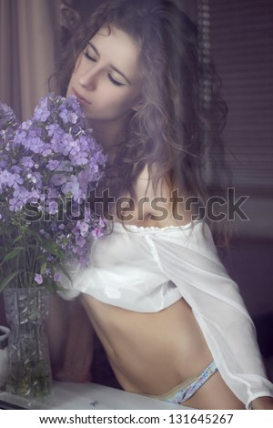 Beautiful brunette girl in underwear lowers the flowers in the room
