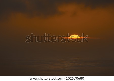 The sun sets across the Irish Sea at Hoopers Point near Skomer on the Pembrokeshire coast. A bank of dense sea mist sits above the horizon.