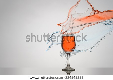 Red and Blue liquid splashing against a glass of red wine on a counter top.