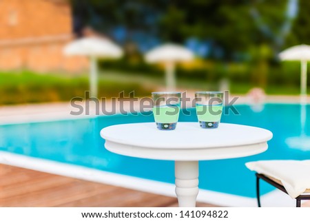 two drinks on a white table with a swimming pool as background