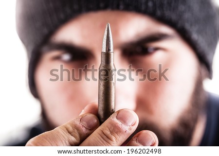 a bearded man wearing a beanie hat holding a sniper bullet and looking at it. Isolated over white