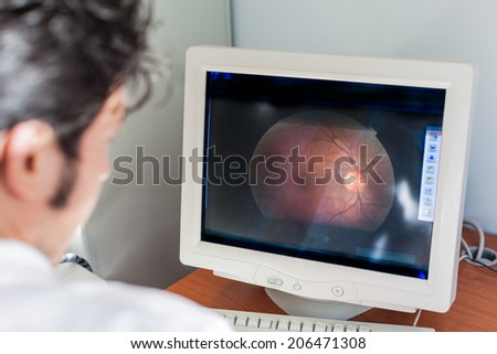 a young ophthalmologist looking at a retina scan in a computer monitor