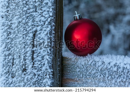 a shiny red christmas ball resting on a wooden fence covered with hoarfrost ice crystals