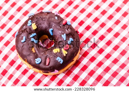 a delicious chocolate donut topped with sugar letters over a classic red and white tablecloth