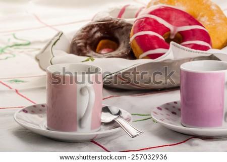 breakfast setting with colorful donuts and two mugs over a tablecloth