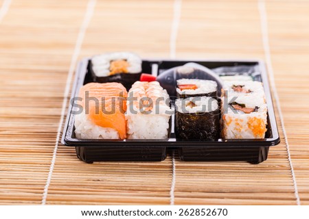 a sushi take away plastic tray box on a wooden bamboo sushi mat