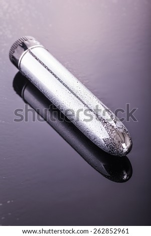 a wet shiny metallic dildo vibrator over a dark reflective surface