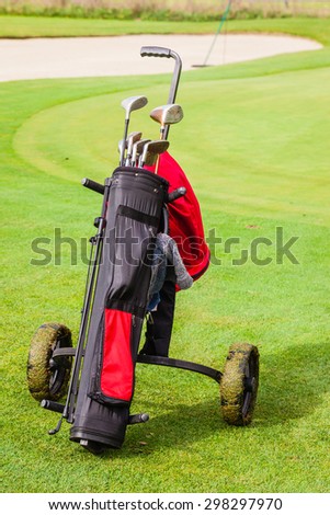 a wheeled golf bag full of golf clubs of a vibrant golf course