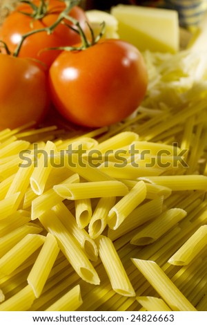 Raw macaroni scattered on a tables with tomatoes and cheese on the background