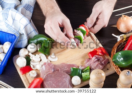 Person making meat sticks over a table full with produces such as bell peppers, pork meat and mushrooms
