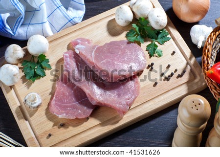 Fresh raw pork meat on wooden board with some fresh veggies around it