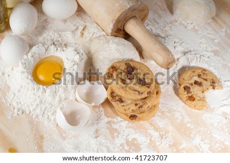 Overhead shot of a few cookies , raw egg and wooden rolling pin