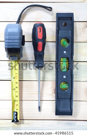 Close up of tape-measure, screw-driver and level onw ooden table top