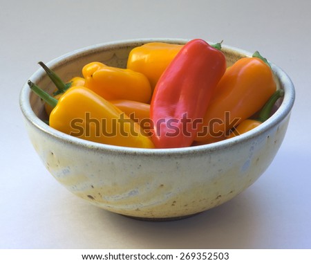 Peppers in a Ceramic Bowl: Red and yellow peppers are arranged artfully in a beautiful ceramic bowl on a white background.