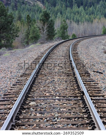 A Railroad of the Wild West. This is a shot taken center stage of the shiny rails on the railroad tracks looking towards tree covered mountains of the western US.