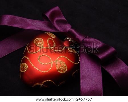 A violet satin ribbon tied in a bow over red hearts a pure black background.