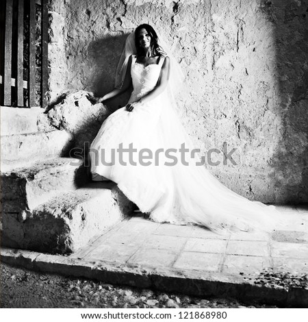 Young bride leaning at a rough wall in Scopello, near Castellammare del Golfo in Sicily, Italy. Black and White.