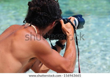 A professional photographer is shooting at the beach. The face is hidden