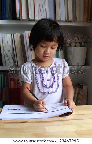A little girl writing or drawing on wooden table.