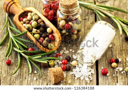 Rosemary, salt and different kinds of pepper on wooden table