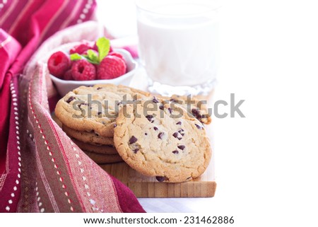 Chocolate chip cookies on a board with milk and fresh raspberries