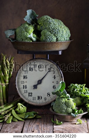 Fresh green vegetables on old kitchen scales on dark background