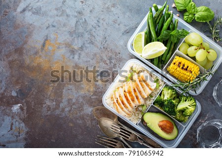 Healthy green meal prep containers with chicken, rice, avocado and vegetables overhead shot with copy space
