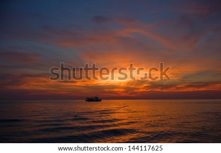 A ferry makes its evening journey on the sea in the rows of the setting sun.