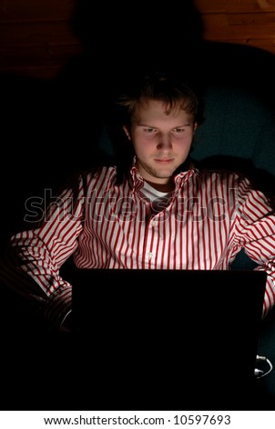 young adult working late at night on his laptop. dark scene and a little mysterious