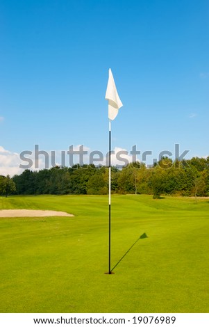 Typical view on a golf course. A generic white flag marking the hole. With a blue sky in the background.
