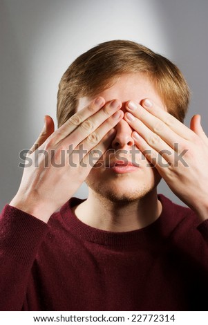 young adult in his 20s covering eyes with hands while having calm look on his face