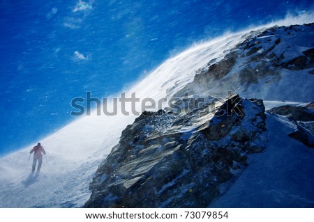 man hiking mountain during snow storm with blue sky