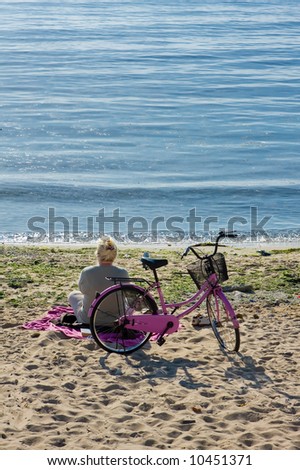 Old woman watching the sea, her pink bicycle is behind