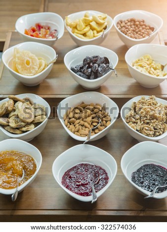 Cereals, nuts and jams in bowls on a wooden table at a hotel breakfast buffet
