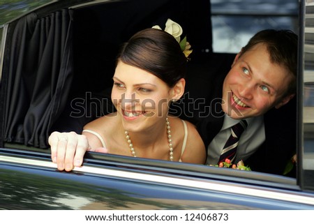 Smiling bride and groom looking out of widow of wedding car limousine.