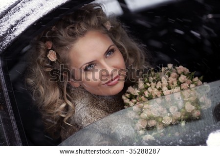 Smiling young adult bride holding bouquet of flowers looking out of limousine window on snowy, wintry day.