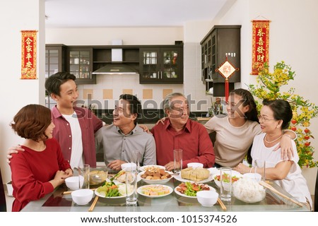Cheerful family members talking at Chinese New Year celebration dinner. Scrolls wishing luck and wealth in the background