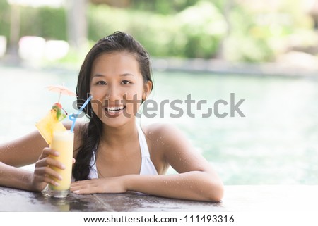 Happy woman with cocktail smiling at camera in swimming pool